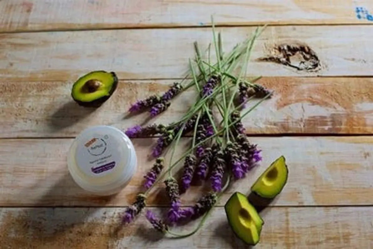 Jar of cream, avocado halves, and lavender on a wooden surface