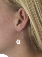 Close-up of a person wearing a silver earring with a pearl drop.