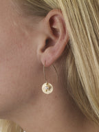 Gold hoop earring with a pearl drop worn by a person with blonde hair.