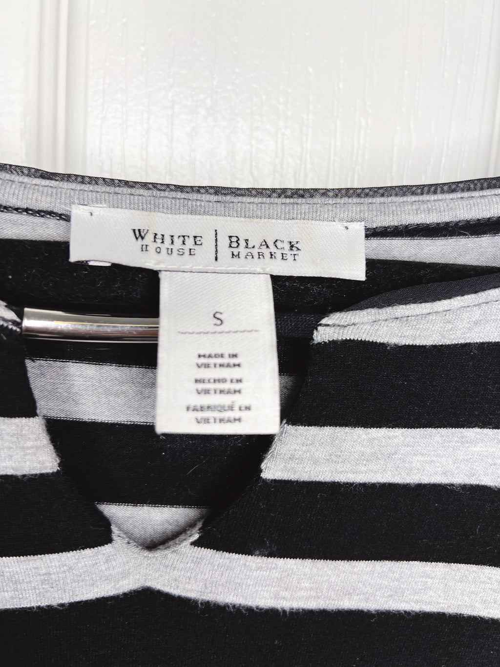 Close-up of a striped knit garment with a visible neck label reading White House | Black Market and a size tag marked S.