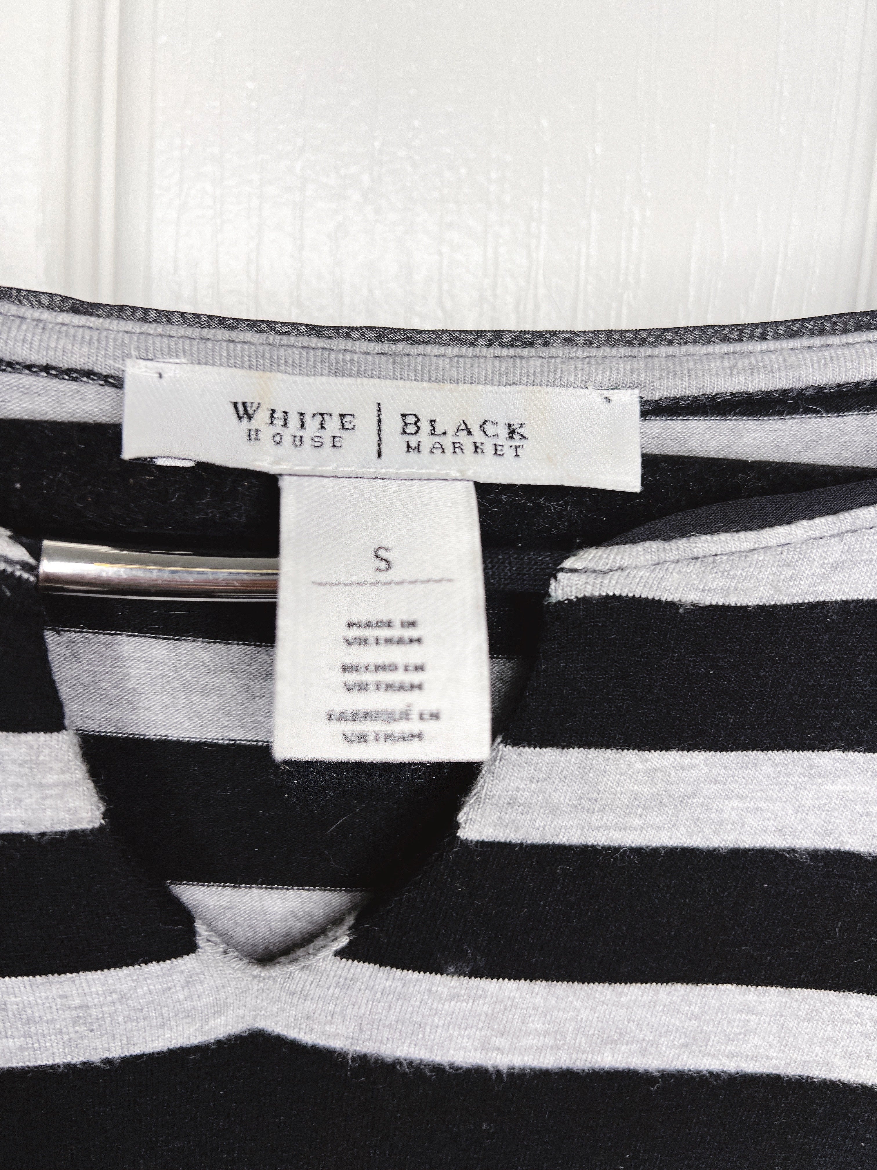 Close-up of a striped knit garment with a visible neck label reading White House | Black Market and a size tag marked S.