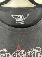 Close-up of a dark gray washed graphic t-shirt hanging on a hanger, showing the inner neck label for the band Sacromania and part of the front graphic print.