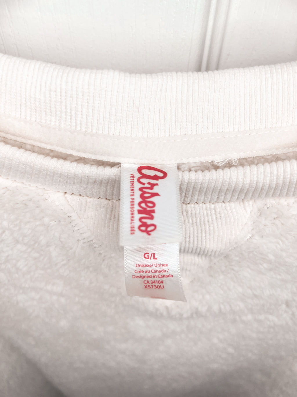 Close-up of a white ribbed sweatshirt neck label with red text reading 'OshKosh' and smaller size information below, set against the white fabric.