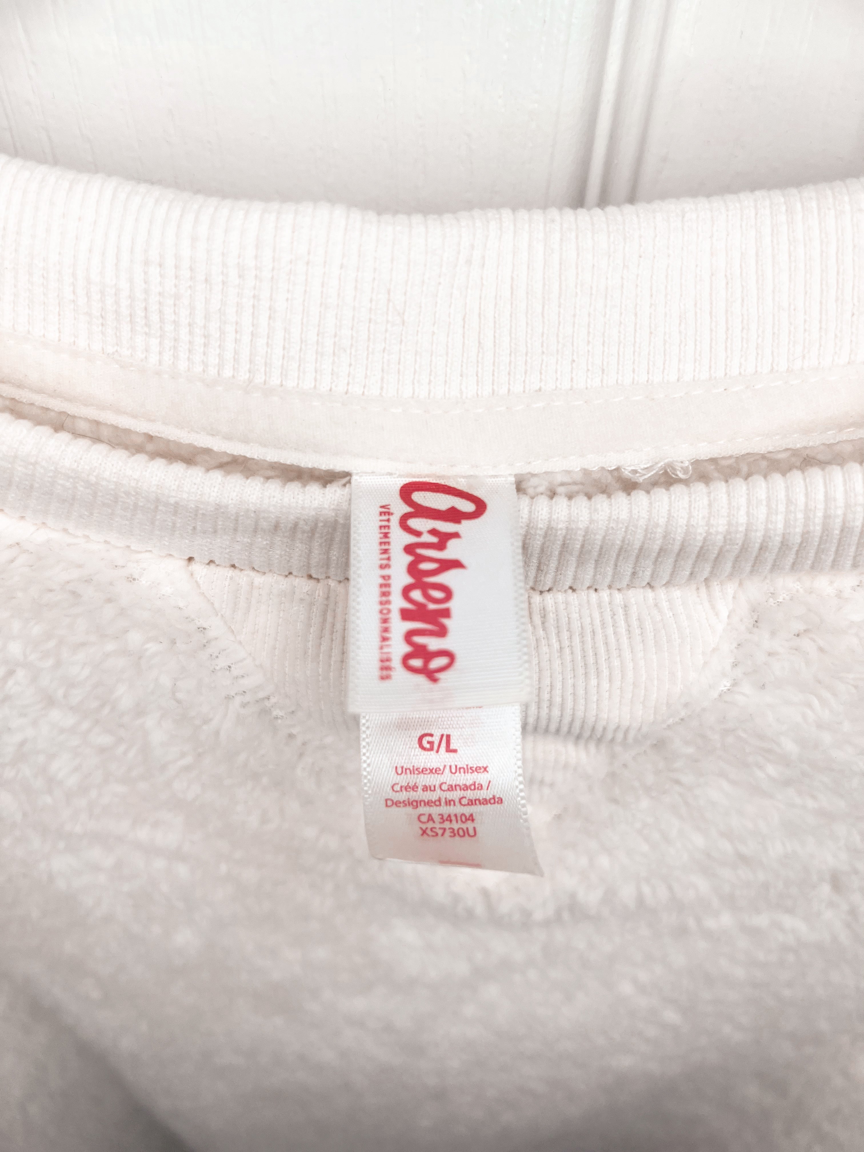 Close-up of a white ribbed sweatshirt neck label with red text reading 'OshKosh' and smaller size information below, set against the white fabric.