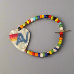Colorful beaded hair clip with a heart-shaped metal piece on a gray background
