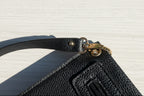 Close-up of a black leather bag with a gold clasp on a textured stone surface.
