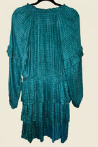 A teal green tiered mini dress with long sleeves and ruffle details, hanging on a black hanger against a white paneled door.