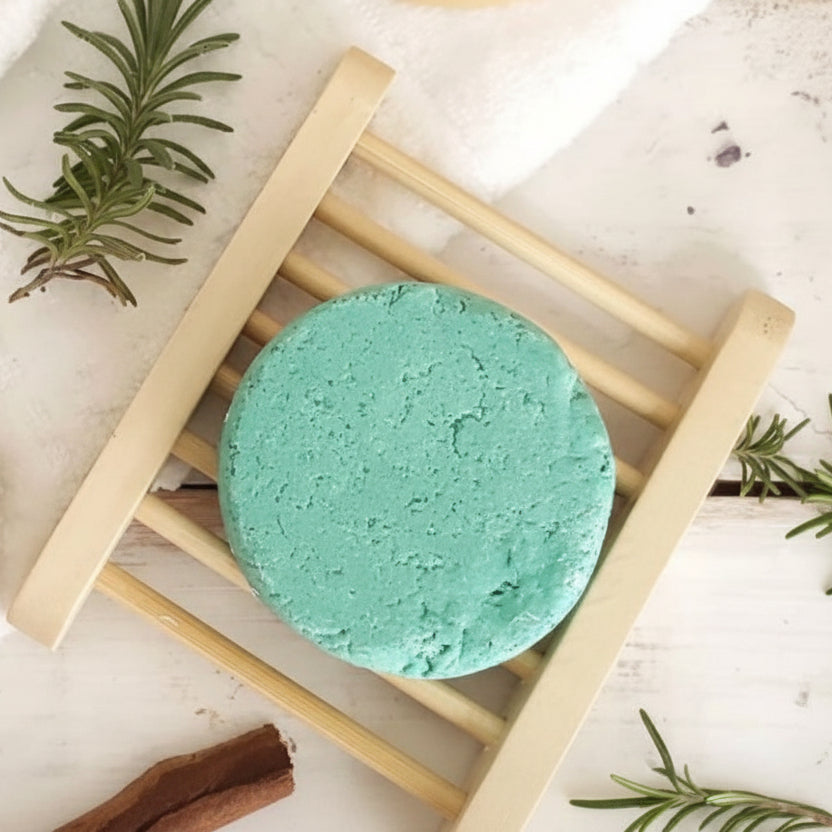Two bath bombs, one green and one beige, on a wooden stand with rosemary sprigs.