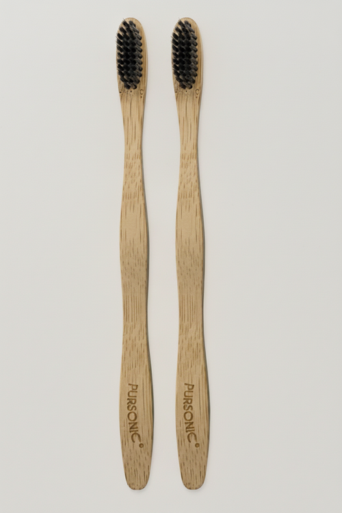 Two wooden toothbrushes with black bristles on a light beige marble background.