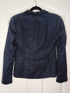 A dark navy blue cropped jacket with a notched lapel collar, shown from the back hanging on a black hanger against a white paneled door.