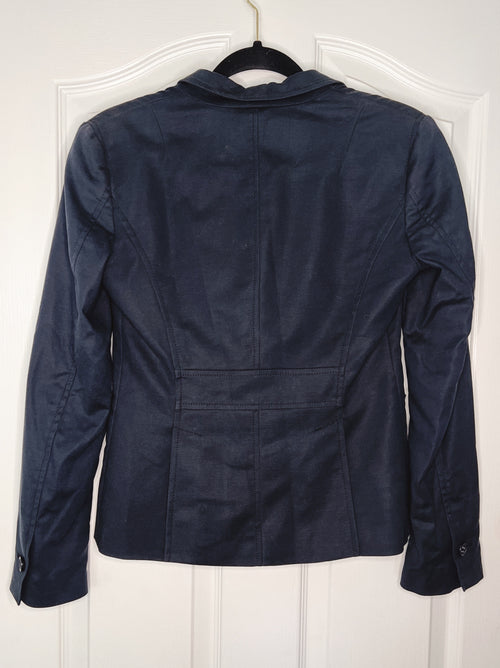 A dark navy blue cropped jacket with a notched lapel collar, shown from the back hanging on a black hanger against a white paneled door.