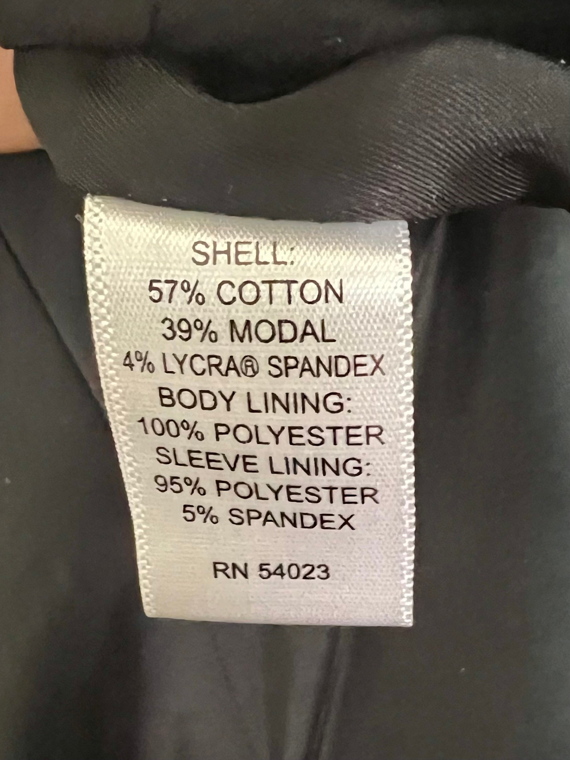 A close-up of a garment's interior care label showing fabric composition details, including shell and body lining percentages, set against a dark black fabric background.