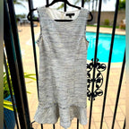 Gray sleeveless dress with ruffled hem on a hanger against a poolside background
