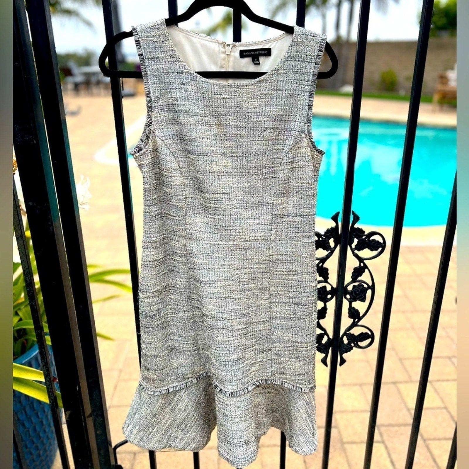 Gray sleeveless dress with ruffled hem on a hanger against a poolside background