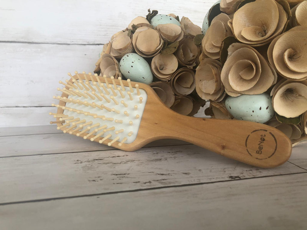 Wooden hairbrush with natural bristles on a wooden surface with decorative eggs and flowers.