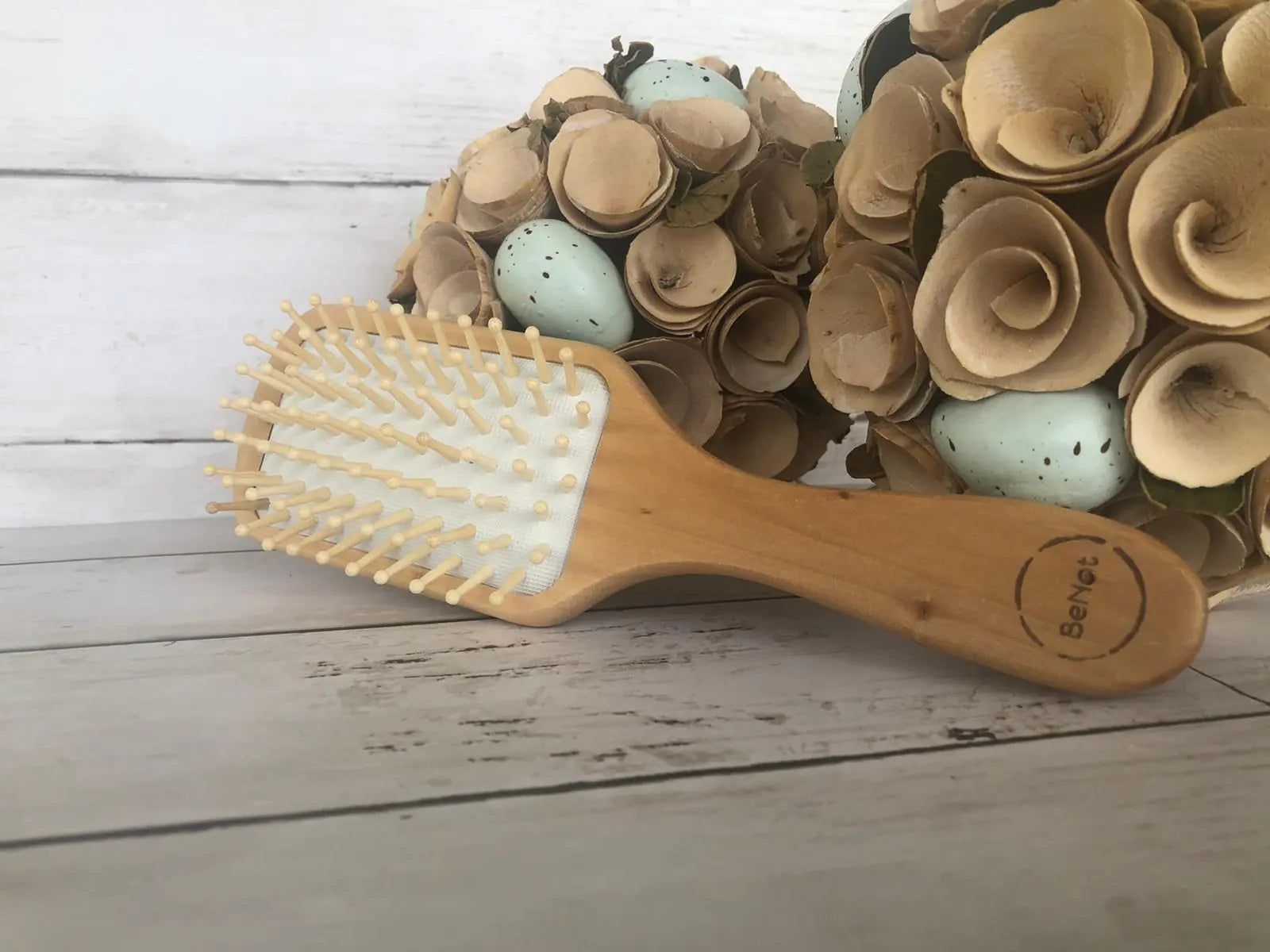 Wooden hairbrush on a wooden surface with decorative eggs and flowers.