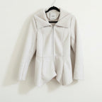 A beige, waist-length Bebe coat with an uneven hem and raw seam detailing, displayed on a hanger.