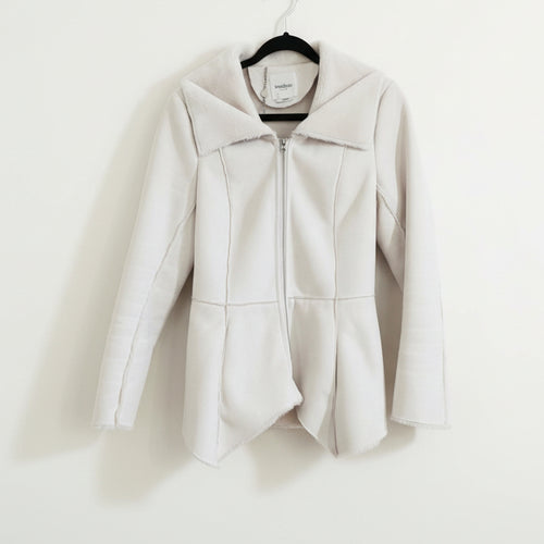 A beige, waist-length Bebe coat with an uneven hem and raw seam detailing, displayed on a hanger.