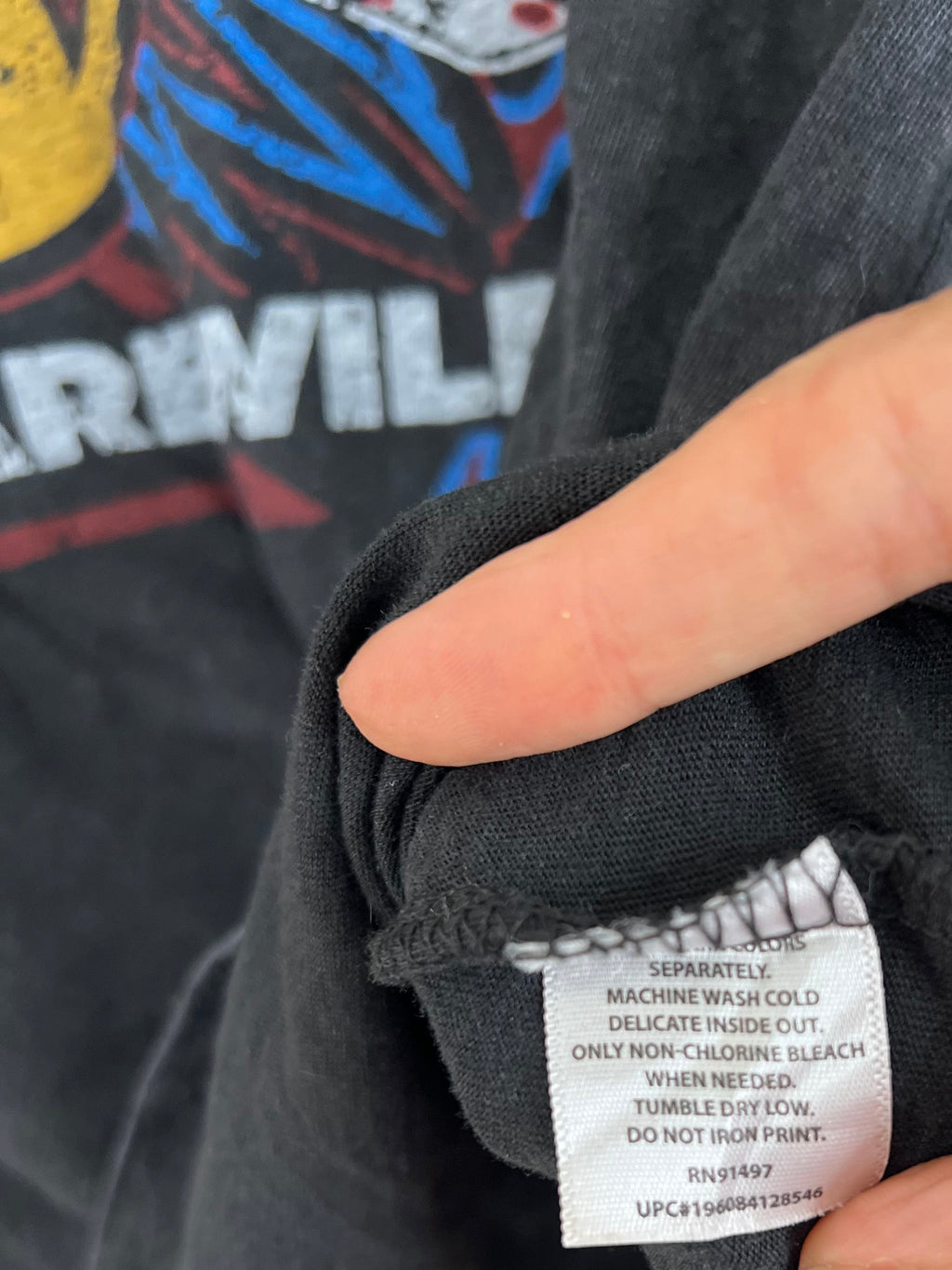 Close-up of a person's hand holding open a black graphic t-shirt to show the inner care label.