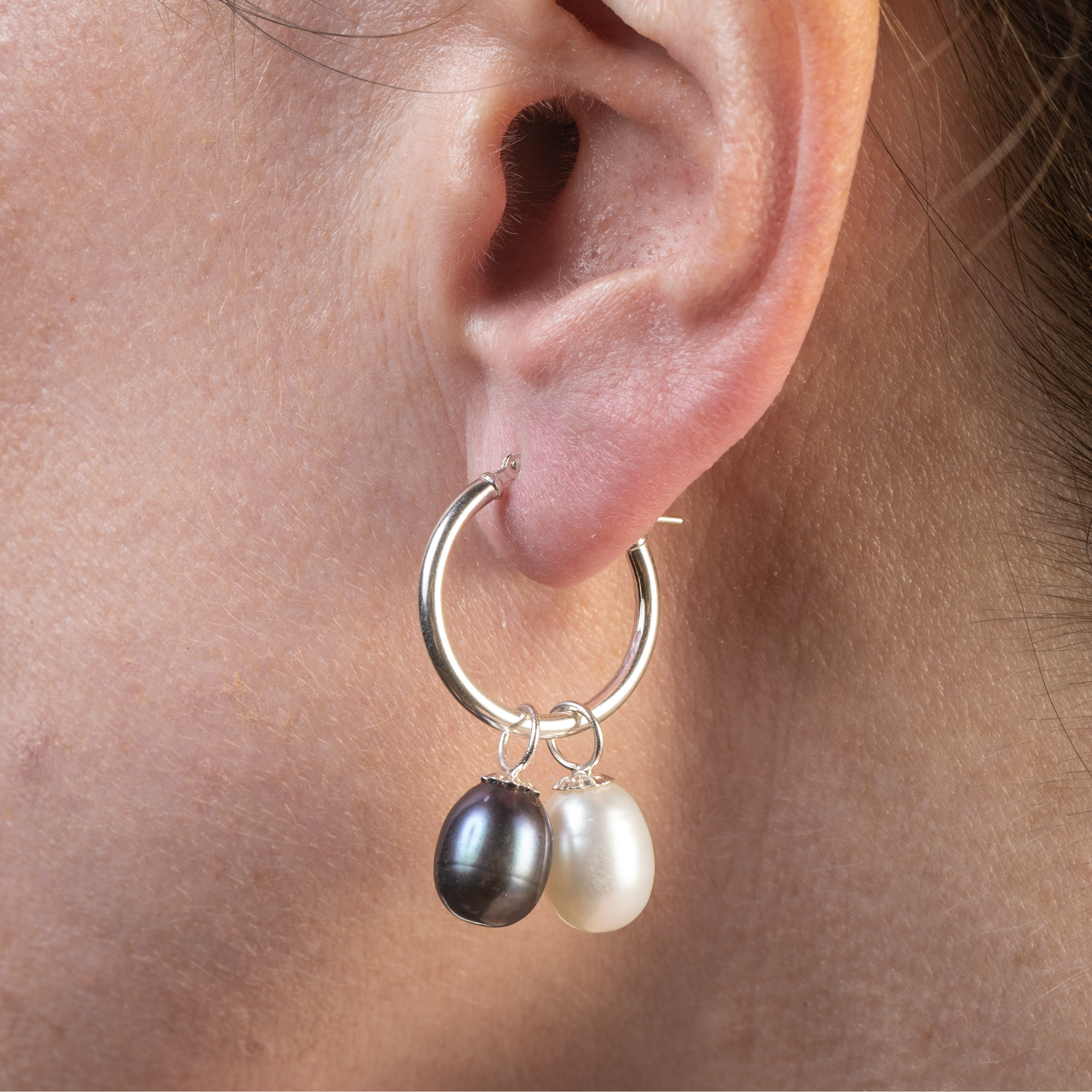 Close-up of an ear wearing a hoop earring with two pearls.