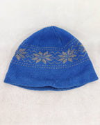 A front side blue knit beanie hat featuring a light beige Fair Isle pattern band across the upper half, laid flat on a light beige textured fabric background.