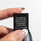 Hand holding a black tag with washing instructions against a concrete background
