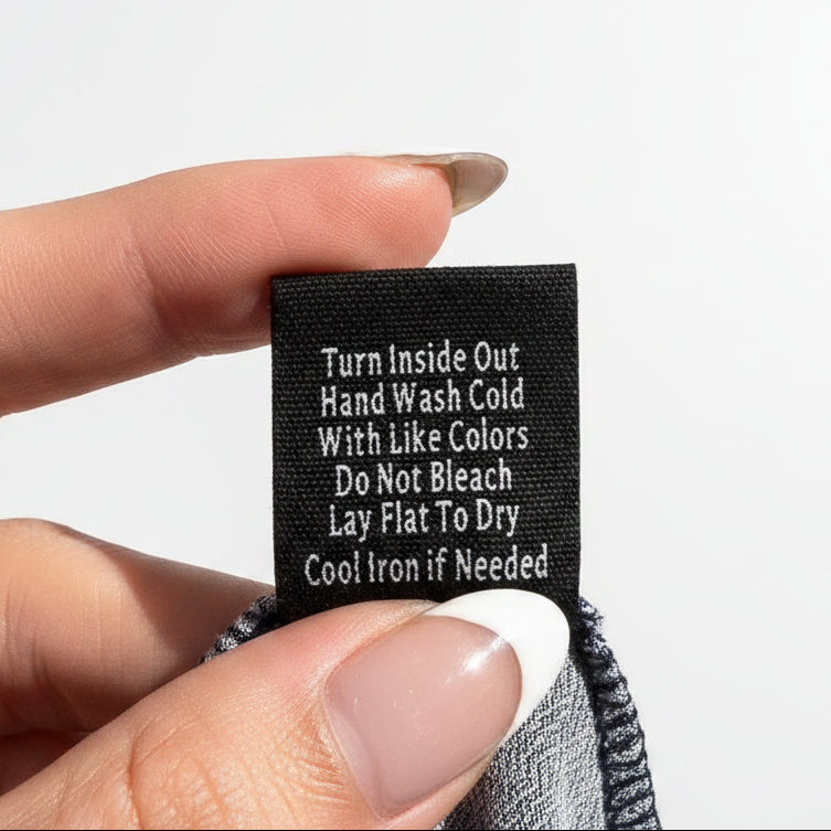 Hand holding a black tag with washing instructions against a concrete background