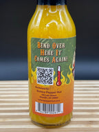Hot sauce bottle with a colorful label featuring text and a QR code on a wooden surface.