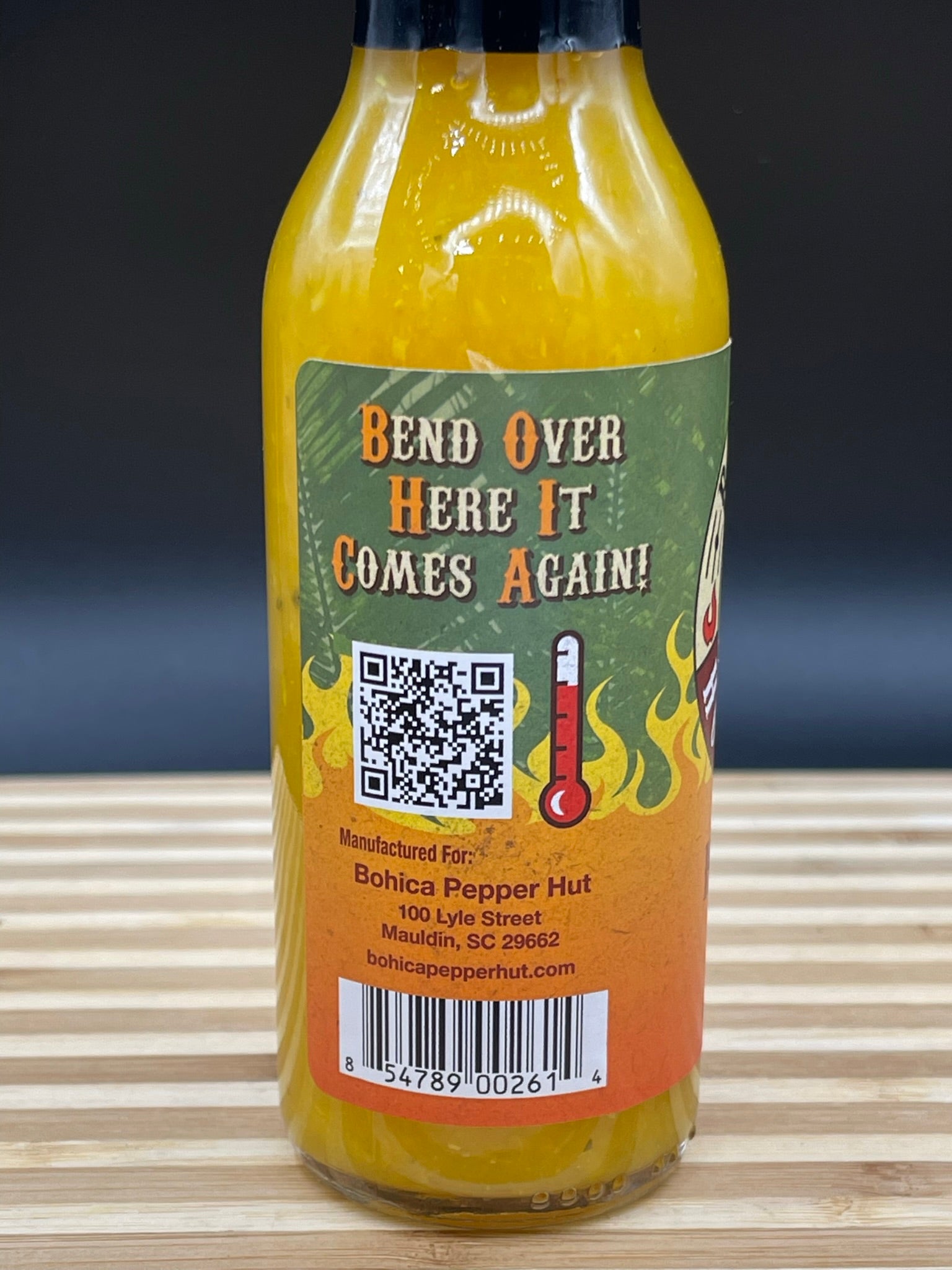 Hot sauce bottle with a colorful label featuring text and a QR code on a wooden surface.