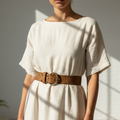 Person wearing a white dress with a brown belt in a bright room with sunlight casting shadows.