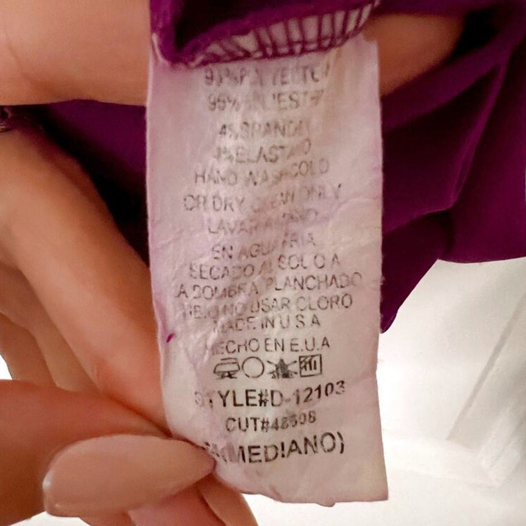 Close-up of a clothing label held by a hand against a white background