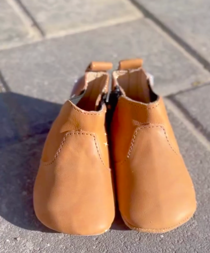 Pair of tan leather baby shoes on a concrete surface