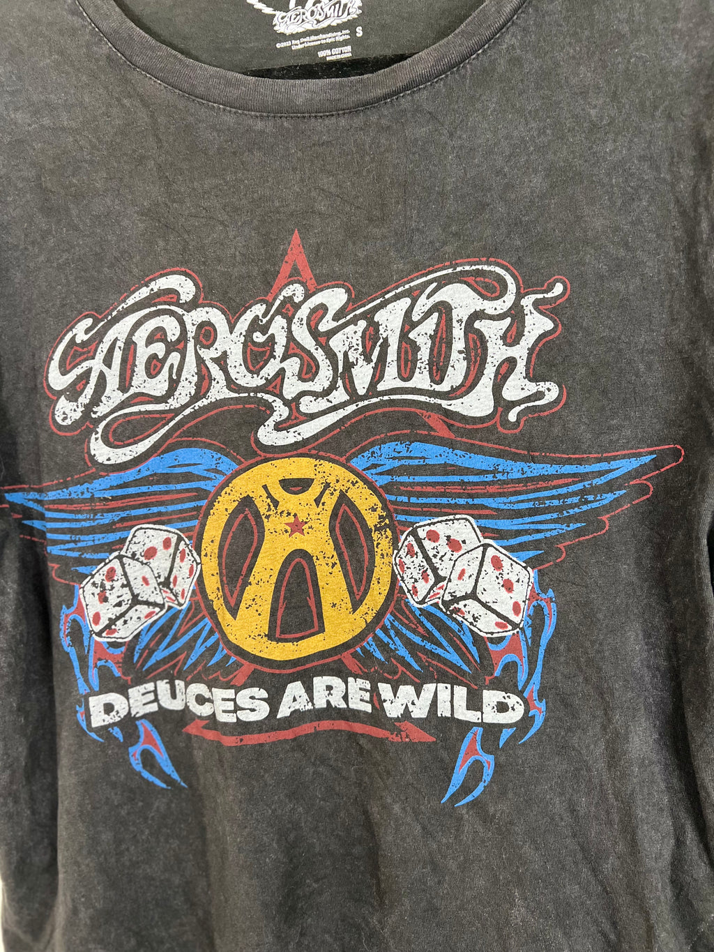 A close-up of a dark gray washed graphic t-shirt featuring the band Aerosmith's logo and 'Deuces Are Wild' print in yellow, blue, red, and white.