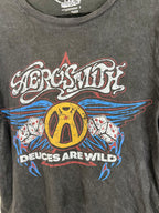 A close-up of a dark gray washed graphic t-shirt featuring the band Aerosmith's logo and 'Deuces Are Wild' print in yellow, blue, red, and white.