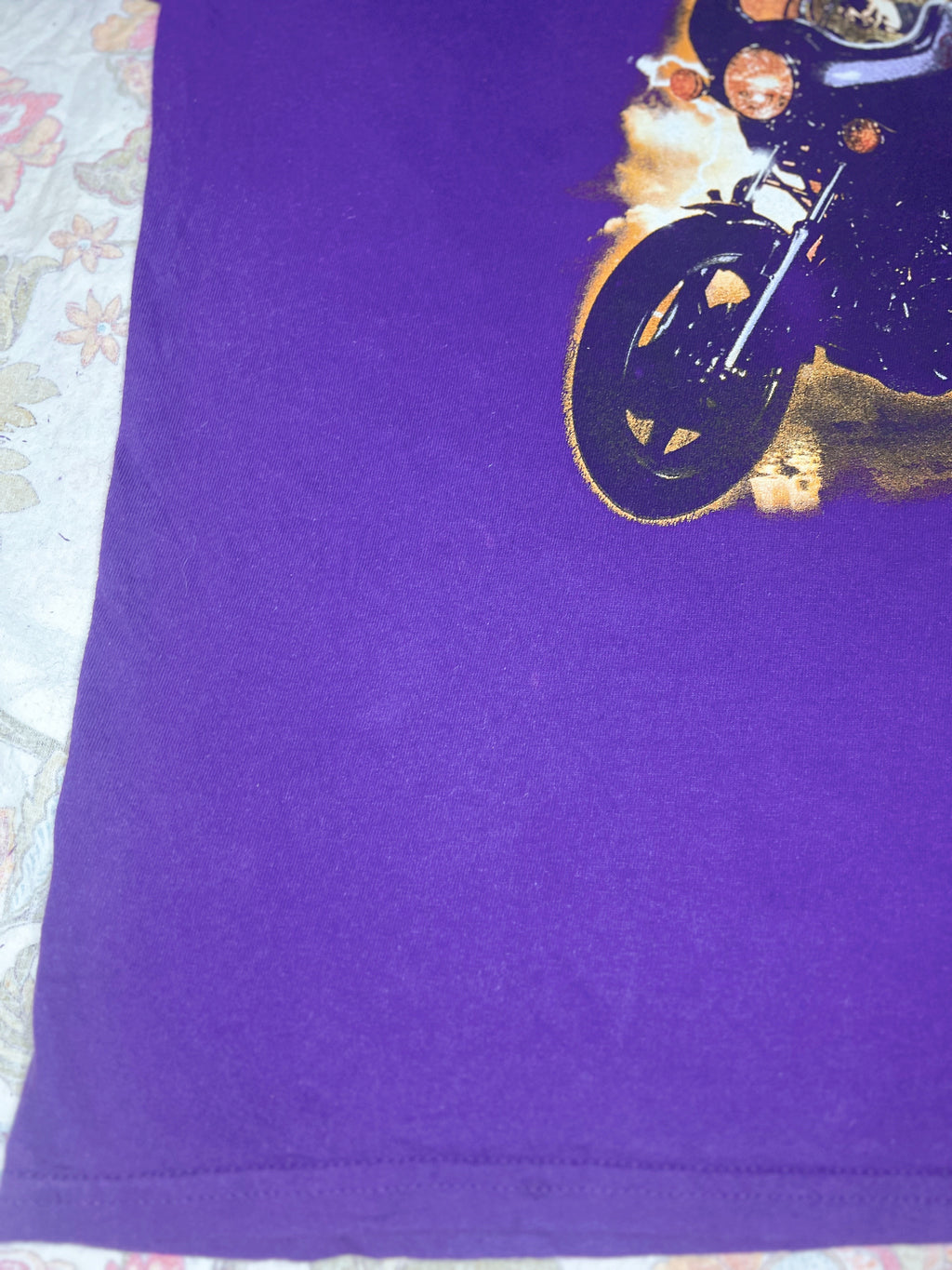 A close-up of a purple t-shirt featuring a graphic print of a motorcycle with flames on the upper right side.