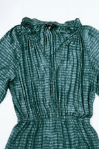 A dark green tie-dye blouse with a textured vertical pattern, featuring a gathered high neckline and short sleeves, shown against a plain white background.