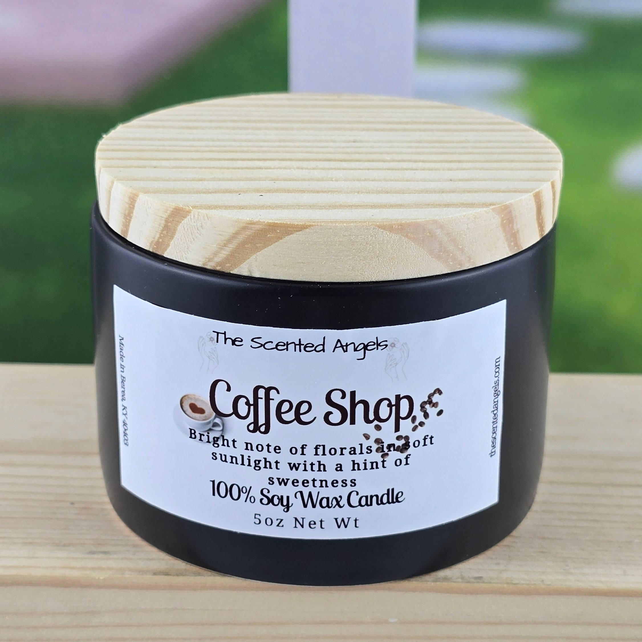 Candle jar labeled 'Coffee Shop' on a wooden surface with a blurred outdoor background