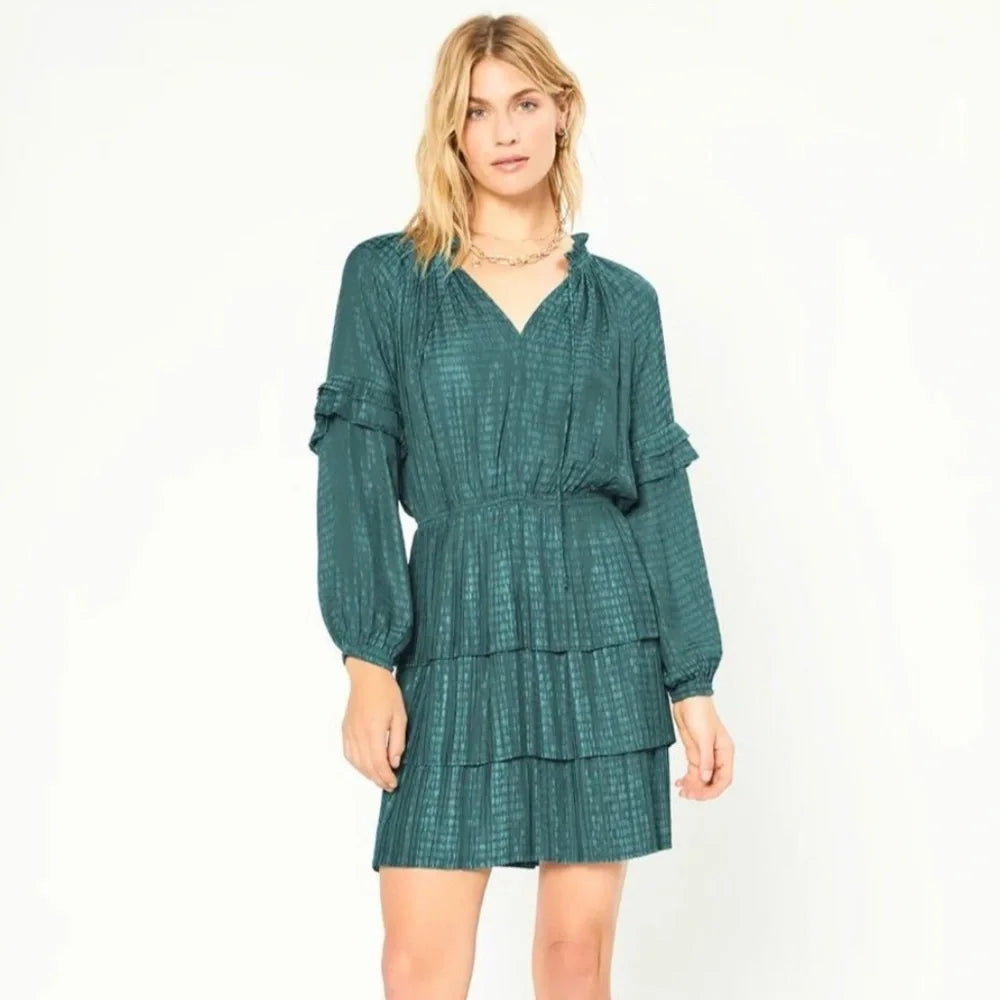 A woman modeling a dark teal green tiered mini dress with long ruffled sleeves and a textured pattern, set against a plain white studio background.