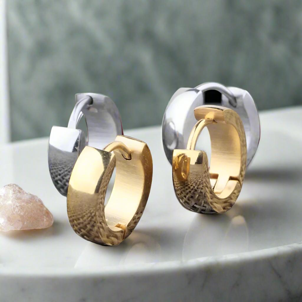 A pair of stackable huggie hoop earrings in silver and gold colors