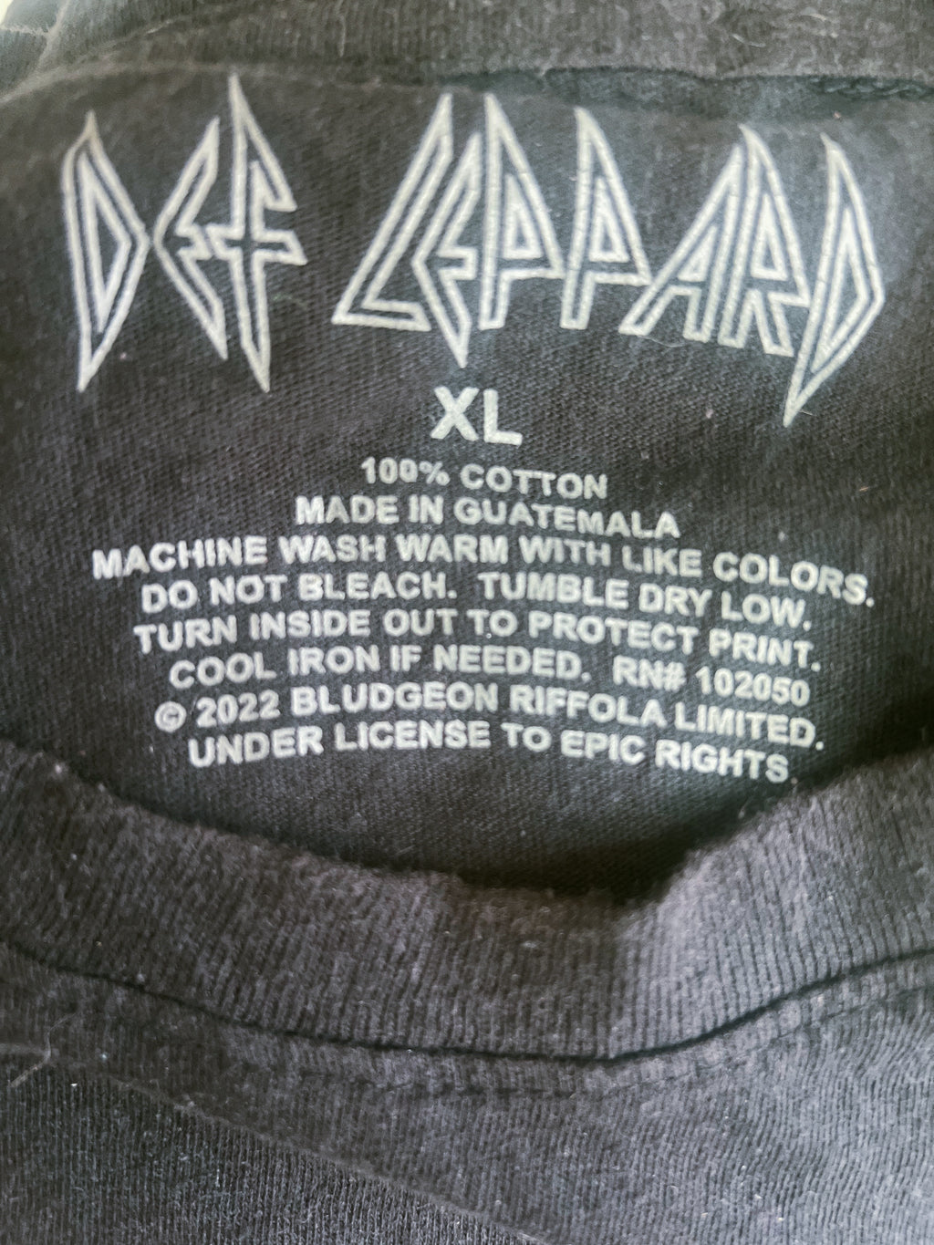 Close-up of the inside neck label of a black Def Leppard XL t-shirt, showing the white printed band logo, size 'XL', and care instructions.