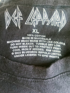 Close-up of the inside neck label of a black Def Leppard XL t-shirt, showing the white printed band logo, size 'XL', and care instructions.