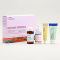 Collection of skincare products including a box labeled 'The Daily Essentials' on a light blue background.