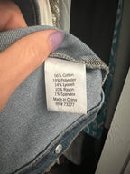 A close-up of a blue denim garment showing the inner care label, held by a hand with lavender-painted fingernails.