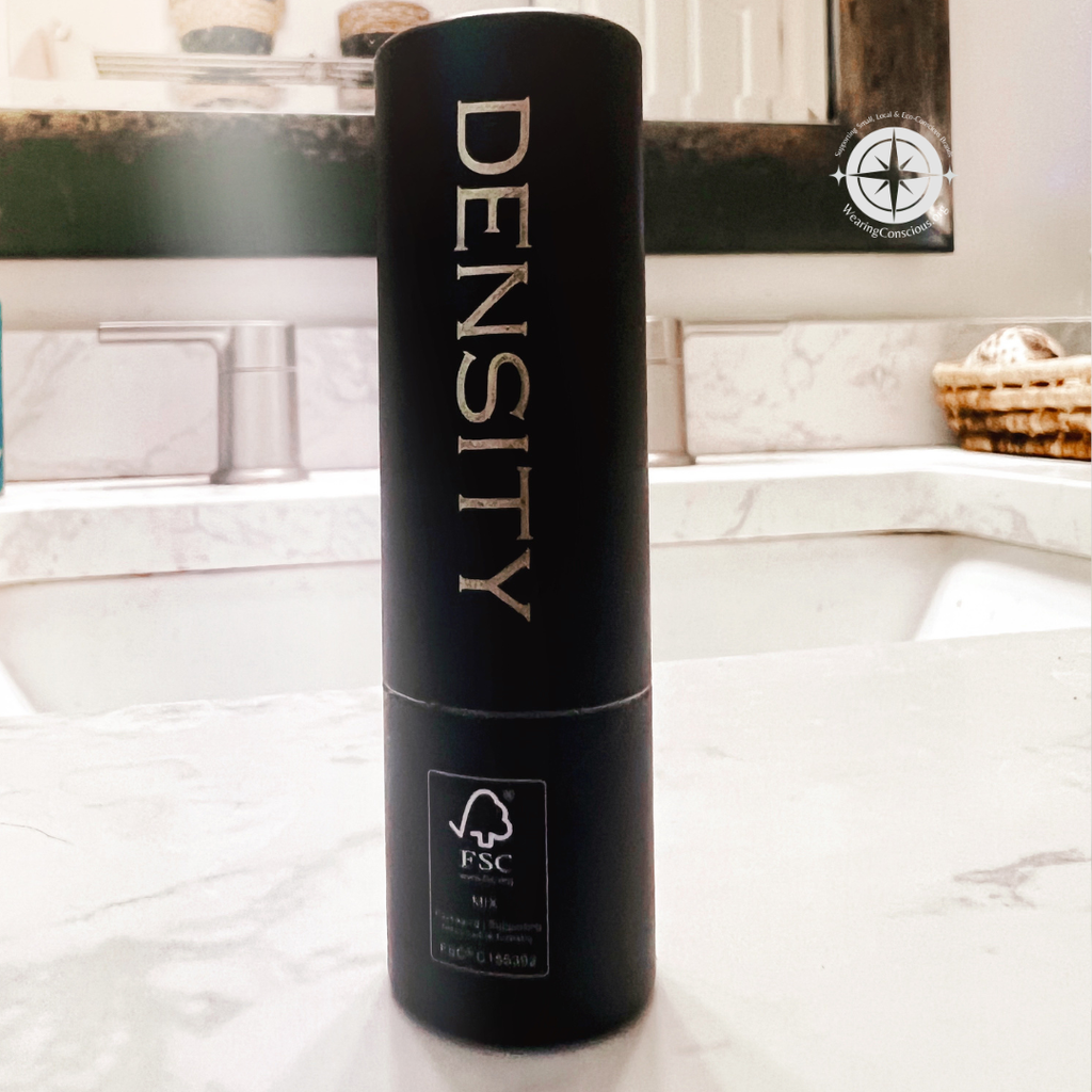 A tall black cylindrical bottle labeled 'DENSITY' with an FSC logo near the bottom, standing on a marble countertop in front of a bathroom sink and mirror.