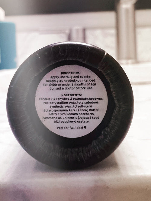 The back of a black jar lid with printed product directions and ingredients on a white label, photographed close-up on a light surface.