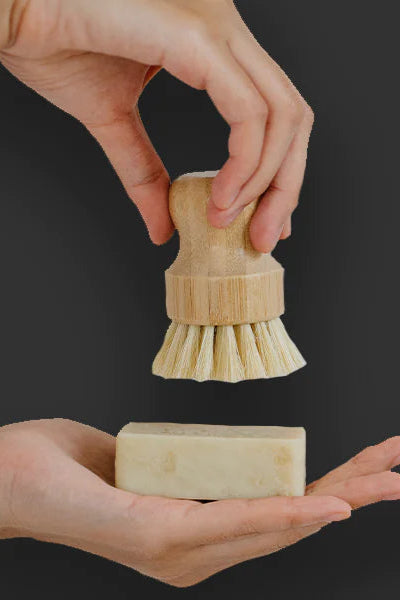 Wooden scrubber and soap held by hands with text about bamboo care on a gray background