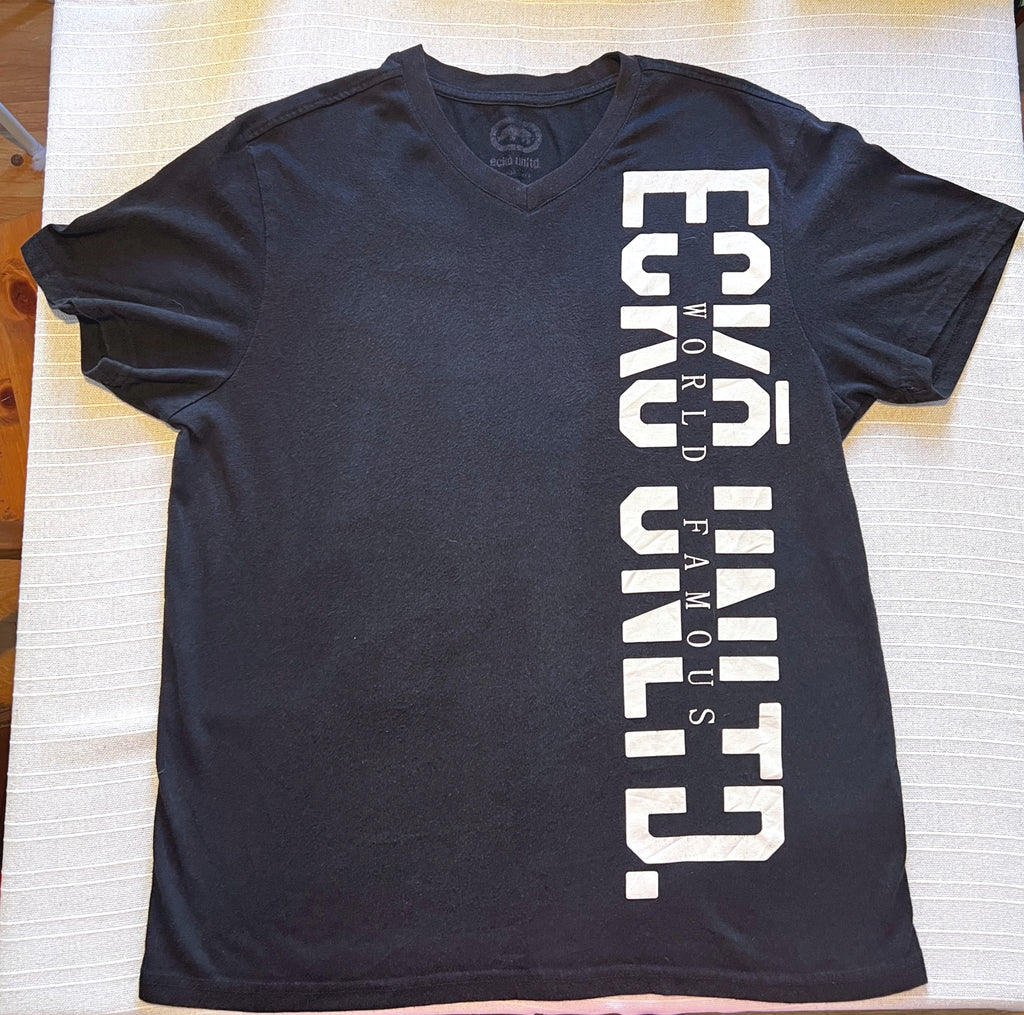 A black short-sleeve V-neck t-shirt with bold white vertical text reading 'ECKO UNLTD' and smaller text 'WORLD FAMOUS' down the right side, laid flat on a light-colored textured fabric surface.