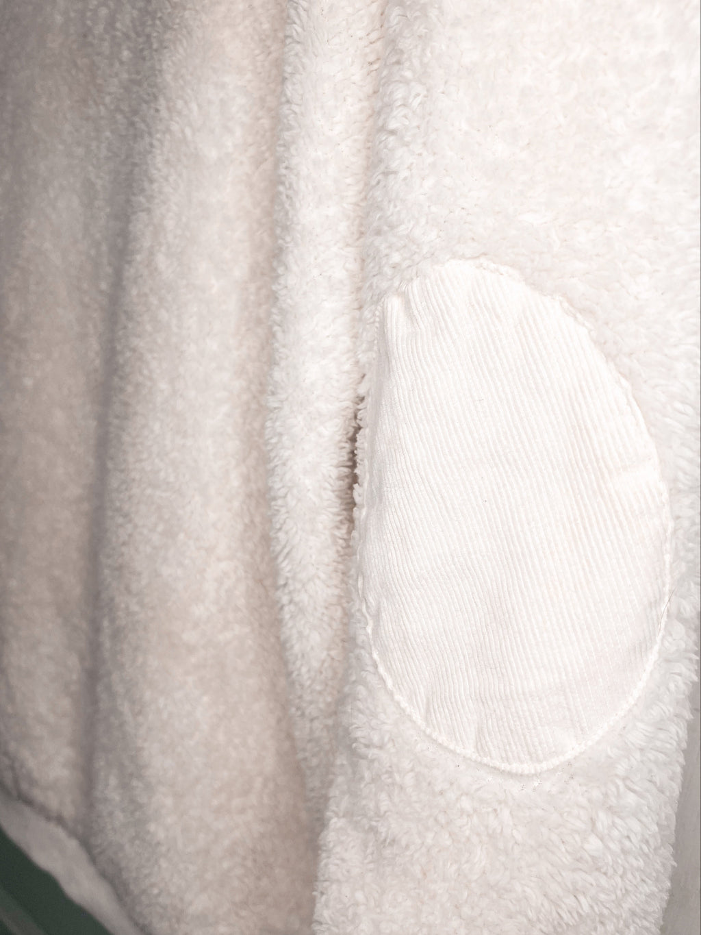 Close-up of a soft off-white fleece or sherpa fabric with a contrasting oval patch of ribbed corduroy texture.