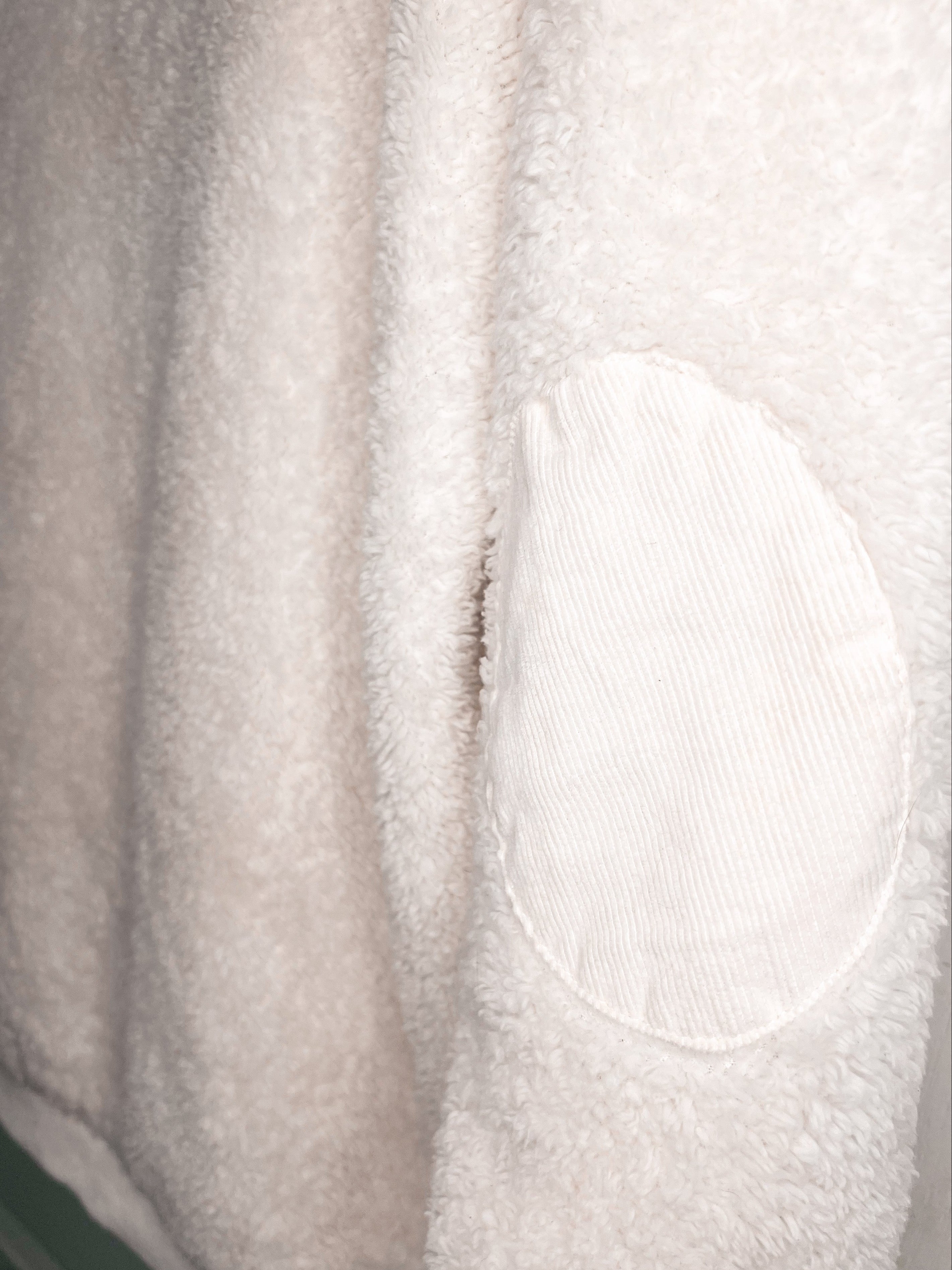 Close-up of a soft off-white fleece or sherpa fabric with a contrasting oval patch of ribbed corduroy texture.
