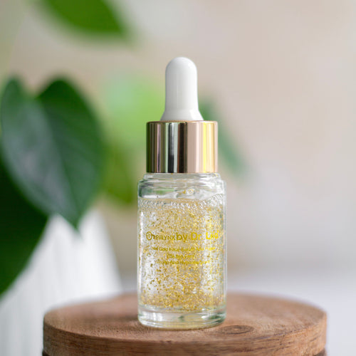 Glass dropper bottle with gold liquid on a wooden surface with a blurred green plant background